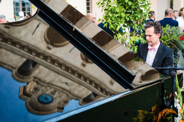 Pianiste en costume jouant sur un piano à queue avec le reflet de la façade de l'Hôtel-Dieu. Photographie corporate à Marseille.