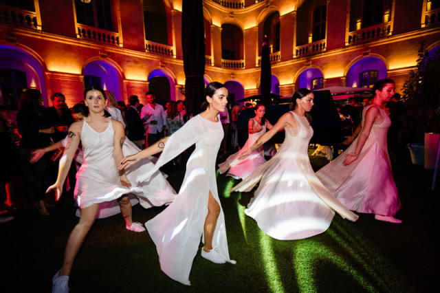 Danseuses en robes blanches fluides réalisant une performance artistique nocturne dans la cour de l'hôtel de luxe à Marseille.