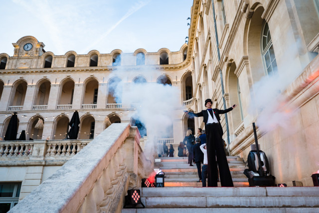Artiste échassier en costume blanc accueillant les invités dans la fumée sur les escaliers de l'hôtel de luxe.