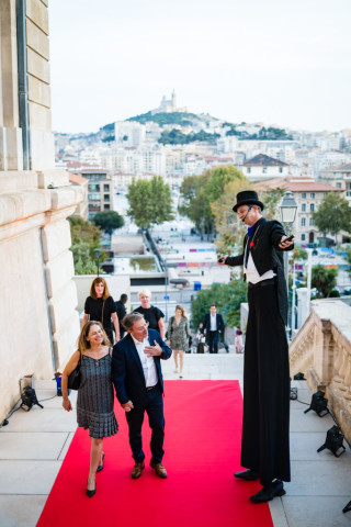 Échassier en costume sombre accueillant élégamment les invités sur le tapis rouge de l'événement.