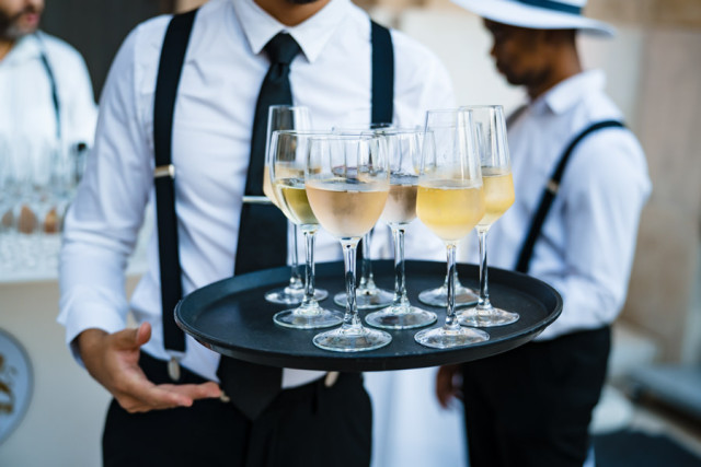 Serveur en tenue portant un plateau rempli de coupes de champagne destinées au toast de la soirée d'entreprise.